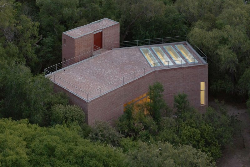 Aerial view of the brick structure with flat roof and clerestory windows surrounded by forested hillside