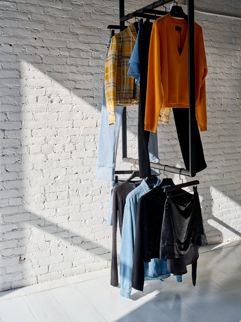 Black metal clothing rack mounted against a white painted brick wall with sunlight casting shadows
