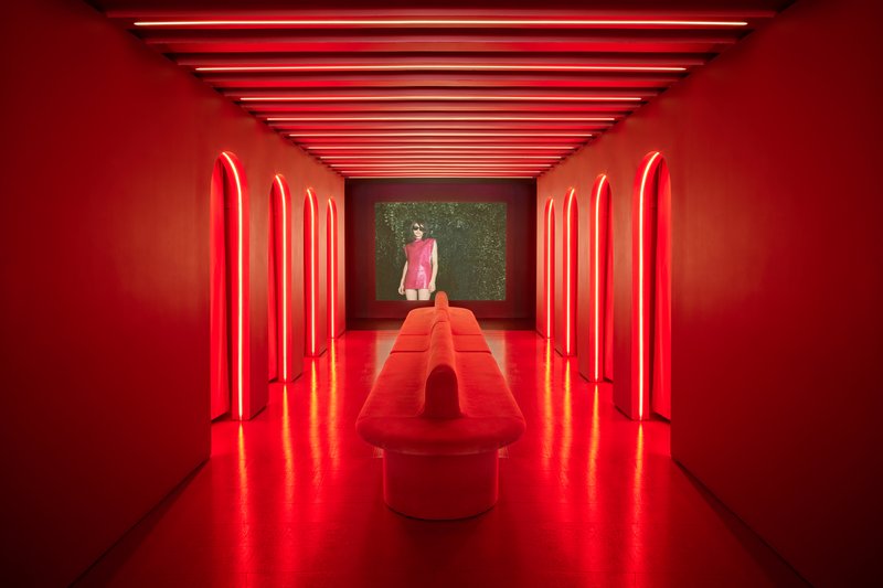 Red neon-lit corridor with arched niches along the walls and a central upholstered bench