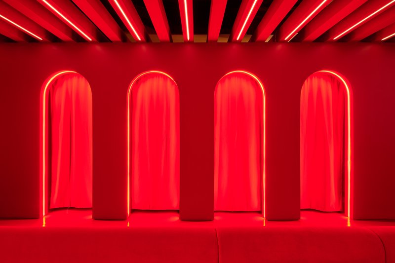 Four arched alcoves with red neon frames and draped curtains along a red-painted wall