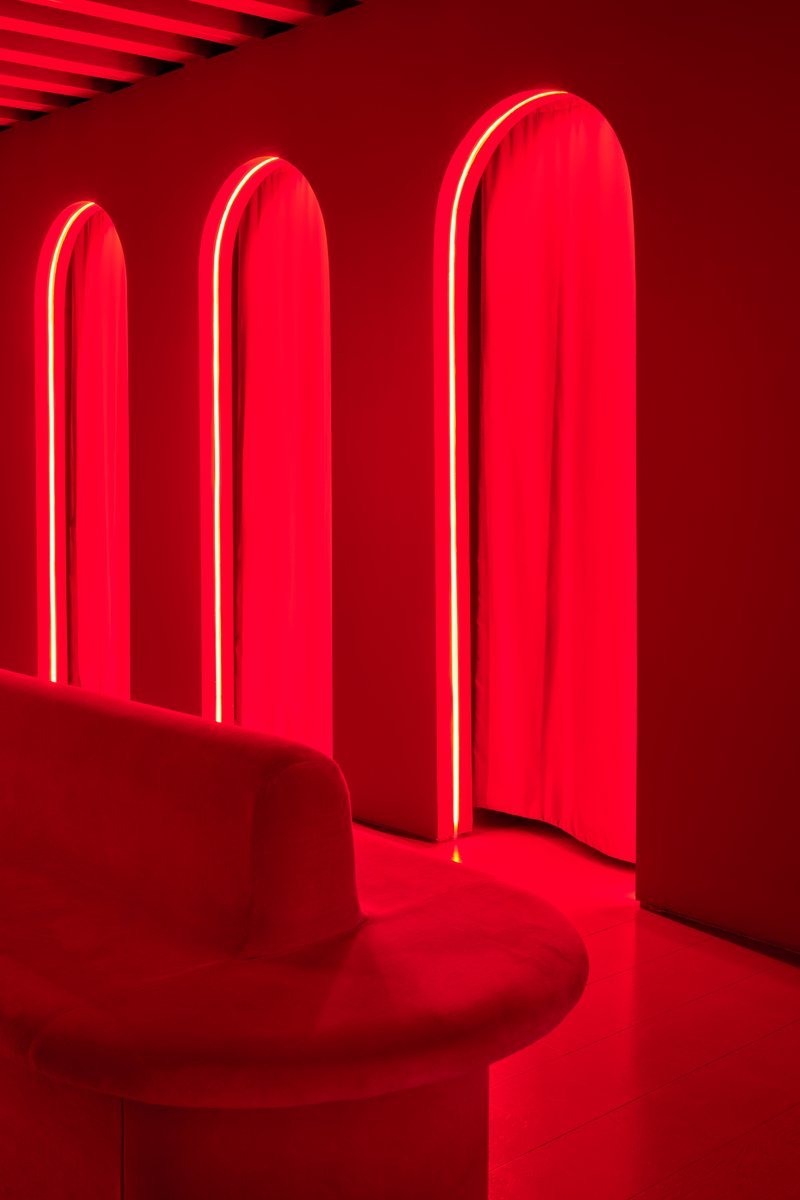 Three red neon-framed arched openings with draped fabric and a circular upholstered seat