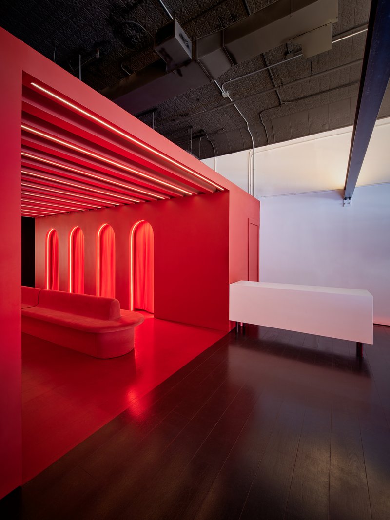 Red upholstered bench against a red wall with illuminated arched niches and exposed concrete ceiling