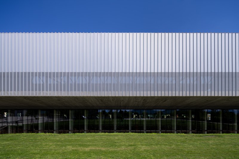 Elevated volume clad in vertical white metal fins above a glazed ground floor and lawn