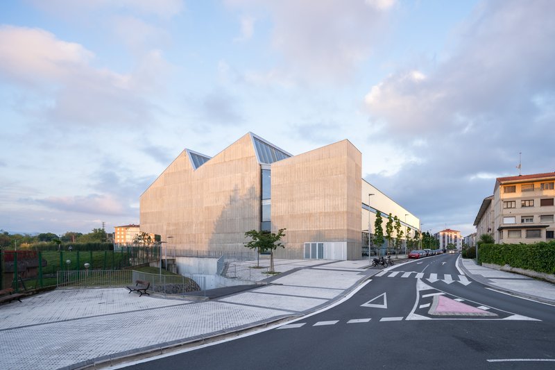 Timber-clad volumes with sawtooth glazed clerestory seen from the street at dusk under cloudy skies