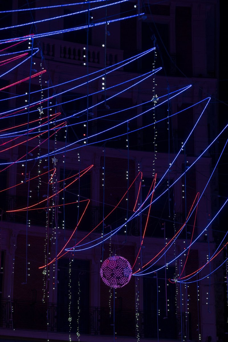 Suspended LED light tubes in red and blue converging toward a spherical purple fixture at night
