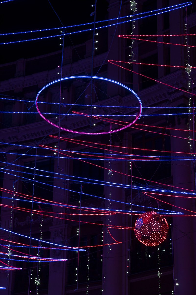 Suspended elliptical light ring with illuminated sphere hanging below among crossing diagonal LED strands