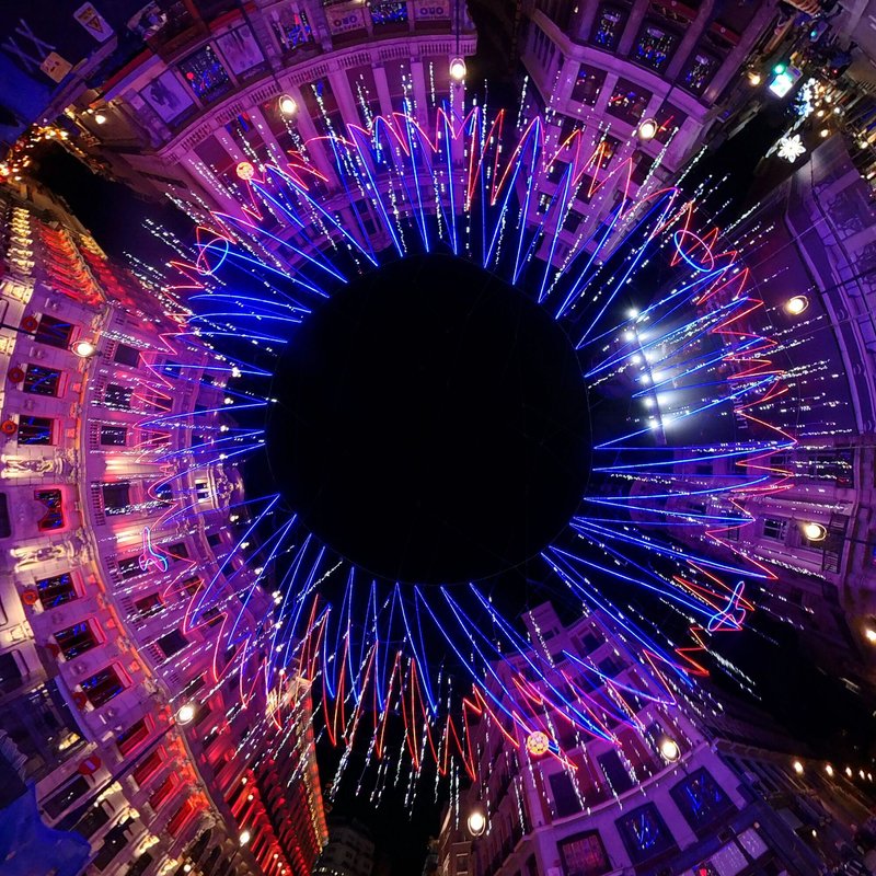 Overhead view into circular courtyard with radiating blue and red LED strands converging toward central void