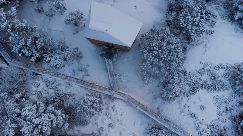 Drone view of the snow-covered volumes and timber walkway through a winter landscape