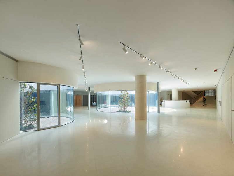 Interior lobby with polished floors, cylindrical column, curved glass wall overlooking a courtyard, and track lighting