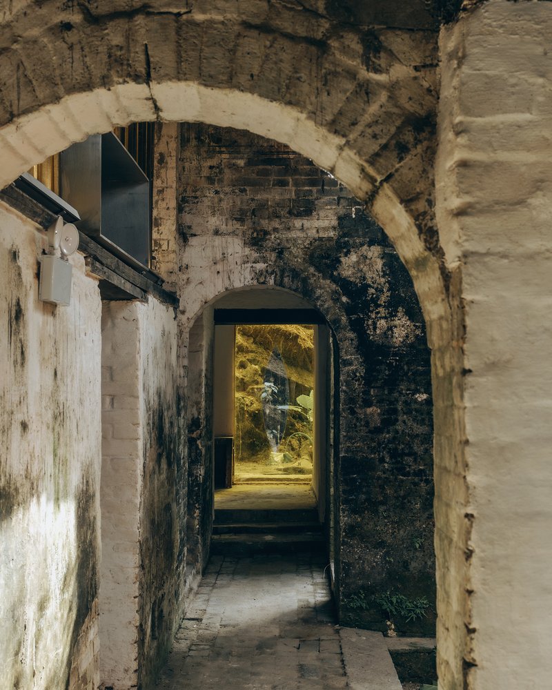 Sequence of brick arches framing a passageway with warm sunlight illuminating the far courtyard