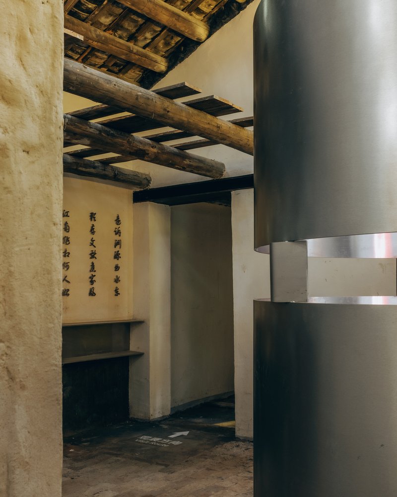 Interior room with exposed timber ceiling beams and a cylindrical metal ventilation duct beside calligraphy panels