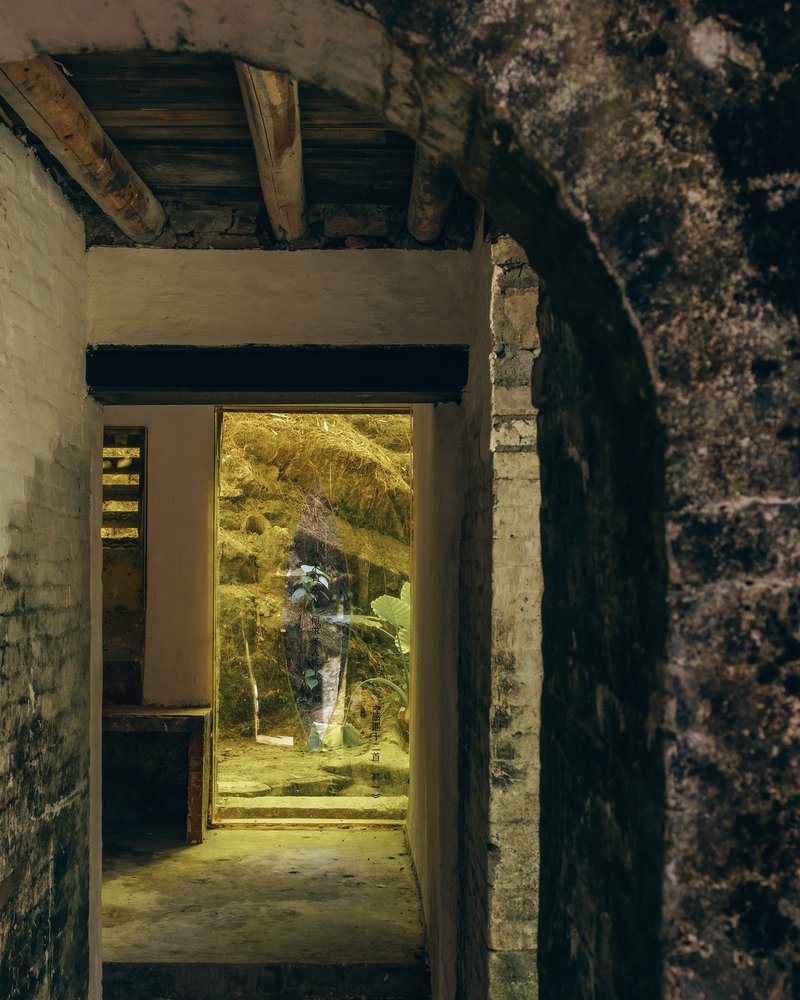 Doorway opening framed by brick archway with warm light spilling onto the threshold and courtyard beyond