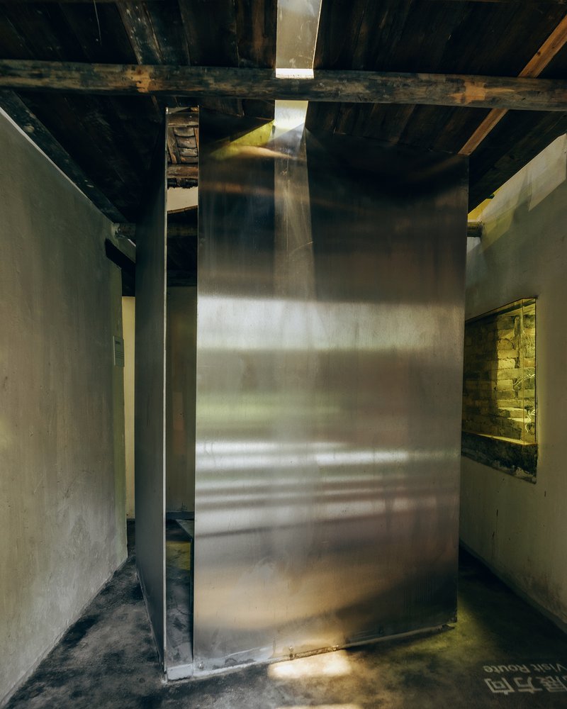 Brass wall panel rising through exposed timber ceiling joists with light from above