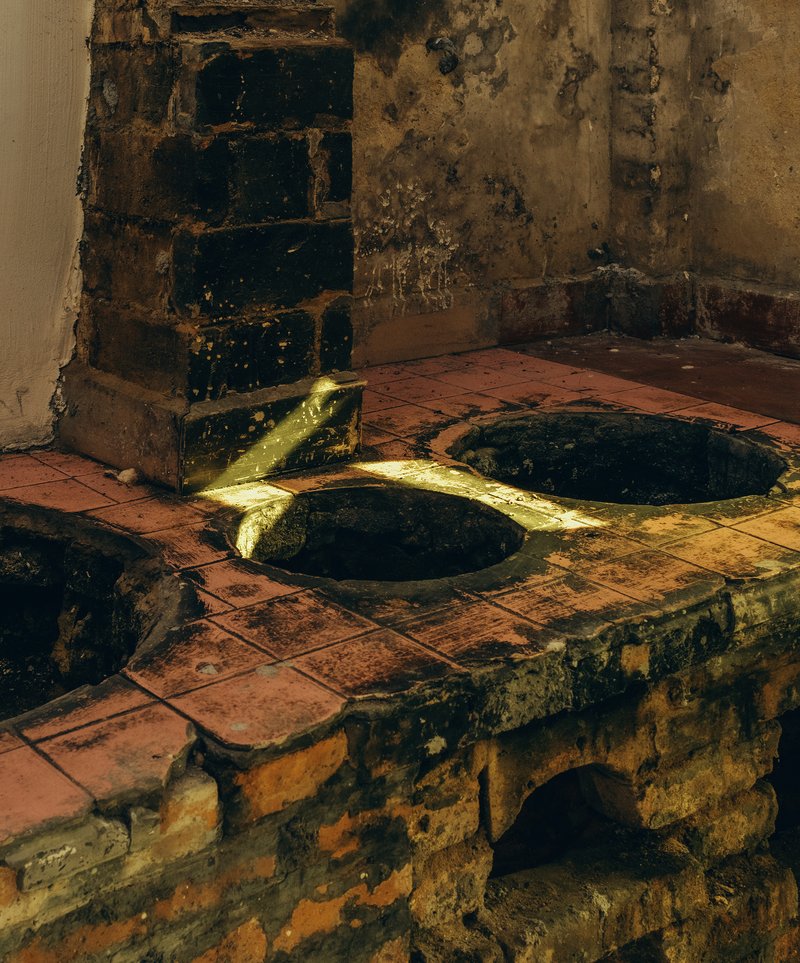 Terracotta tile stove with circular brass burner openings beside a deteriorated wall