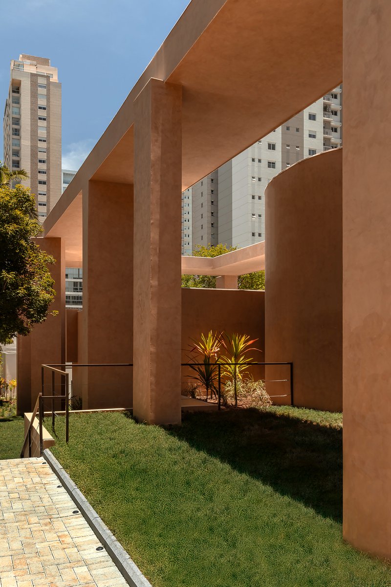 Terracotta columns and beams casting shadows over a lawn courtyard edged with planted beds