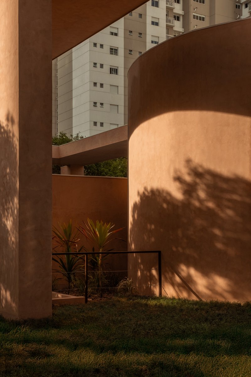 Dappled afternoon shadow of foliage falling across curved terracotta walls beside a lawn