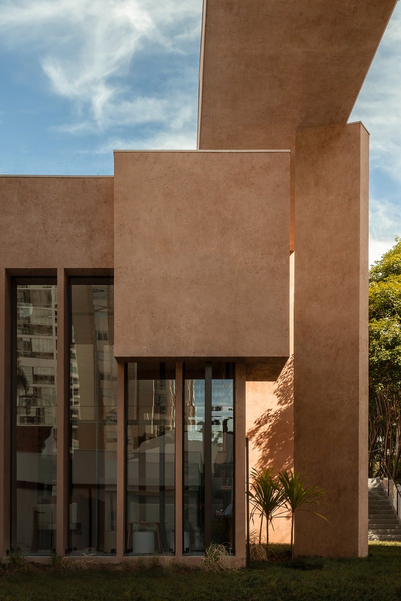 Facade showing cantilevered terracotta volumes above floor-to-ceiling glass walls under blue skies with clouds