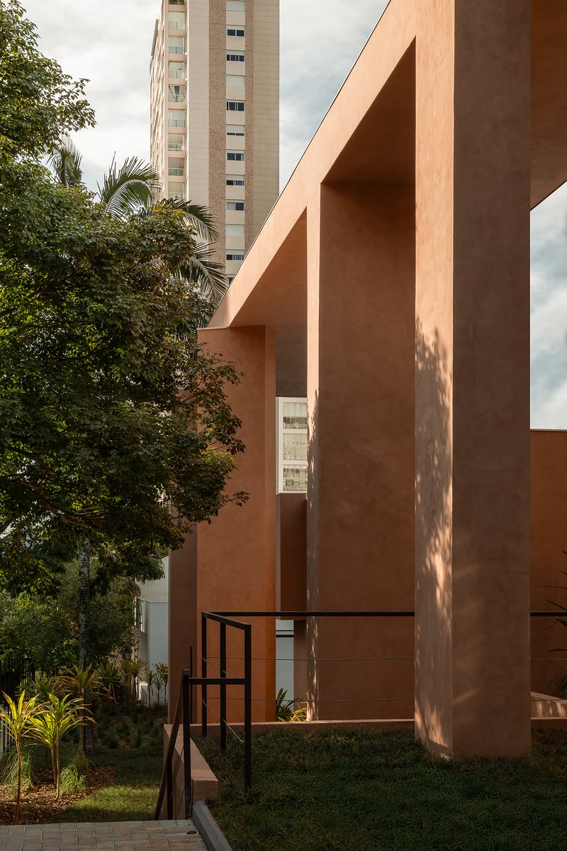 Entry view framed by terracotta columns and beams with metal gate and residential tower behind