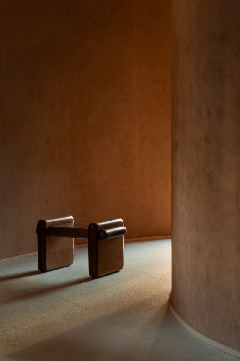 Interior corner with curved terracotta walls and two upholstered stools in warm afternoon light