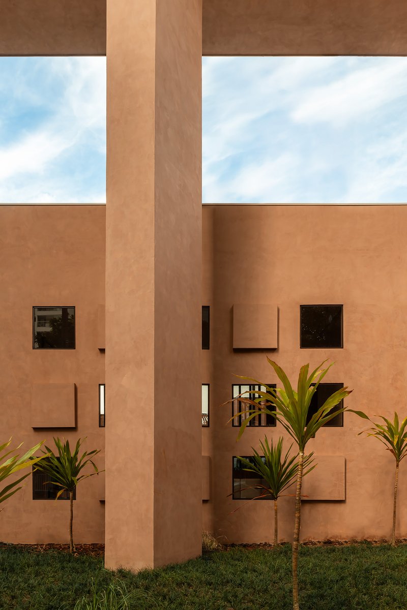Earthen stucco courtyard facade with projecting column, square windows and young palm trees below