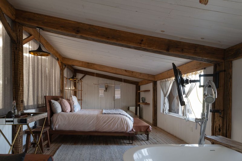Bedroom interior with exposed timber beams, whitewashed plank ceiling and freestanding bathtub beside the bed