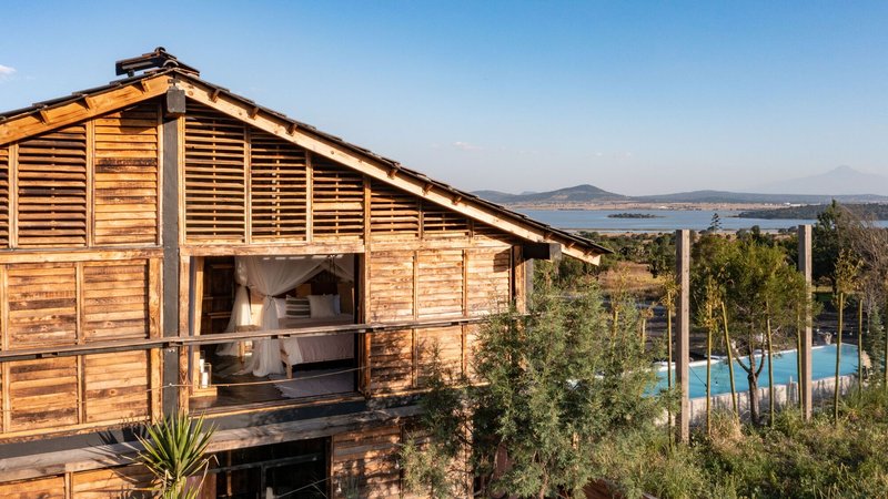 Detail of the slatted wood gable end with open balcony and pool visible through surrounding scrub