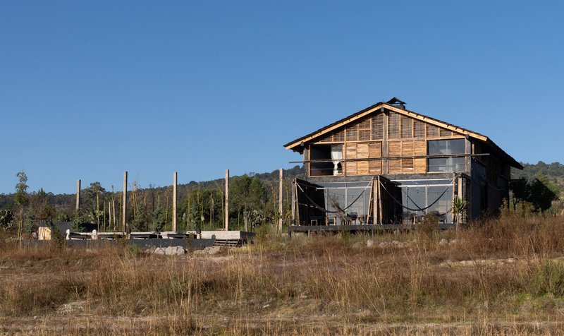 Front elevation showing the gabled timber facade with screened lower porches across a dry grassy field