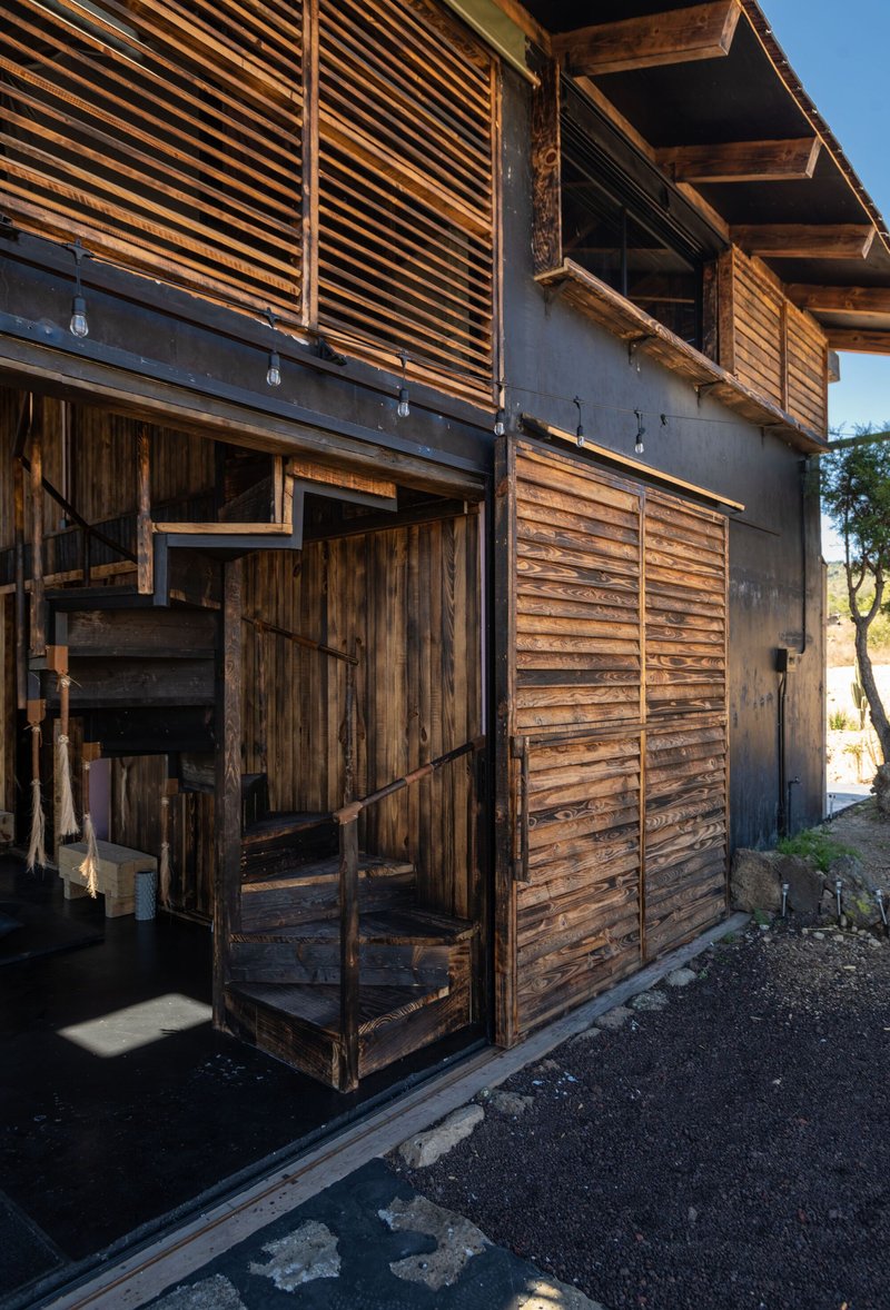 Facade detail showing horizontal timber louvers above concrete band and weathered wooden sliding doors