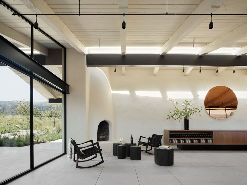 Interior living space with exposed timber ceiling beams, arched fireplace and floor-to-ceiling glazing overlooking the landscape
