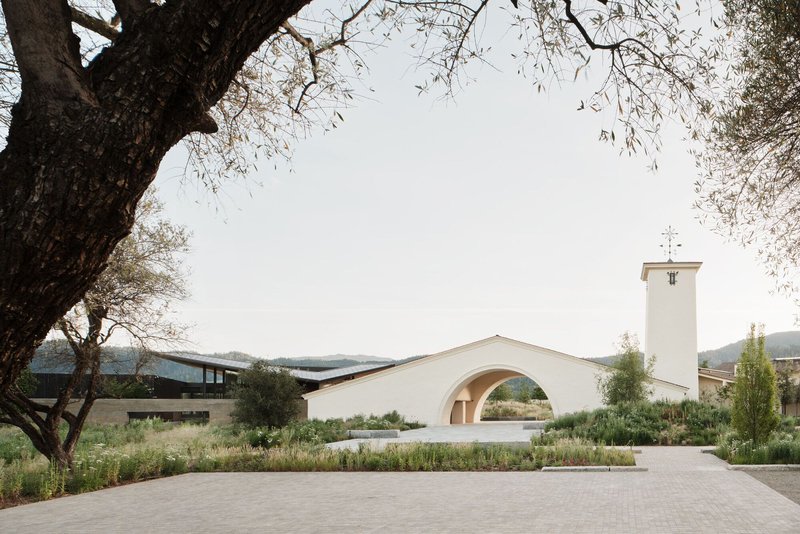 White stucco chapel with bell tower and arched portal seen across native grass plantings