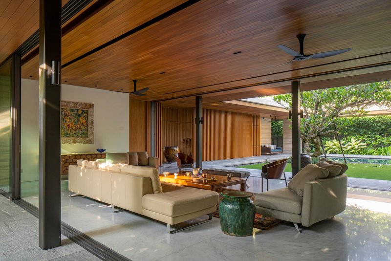 Living room with black steel columns and timber ceiling opening to the garden through full-height glazing