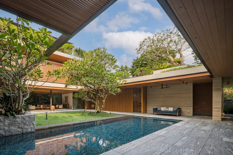 View across the courtyard pool towards the lawn and timber-screened volumes under scattered clouds