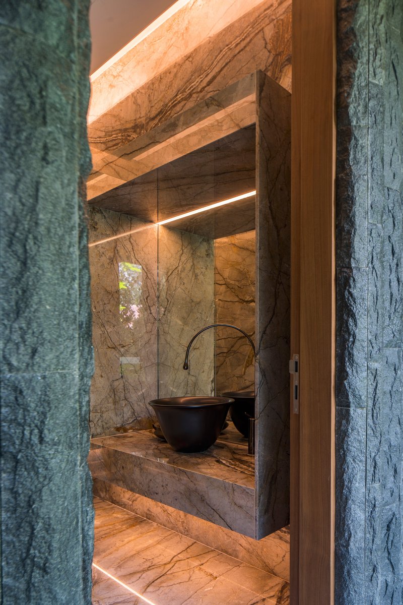 Powder room vanity clad in veined stone with a black vessel sink and backlit mirror