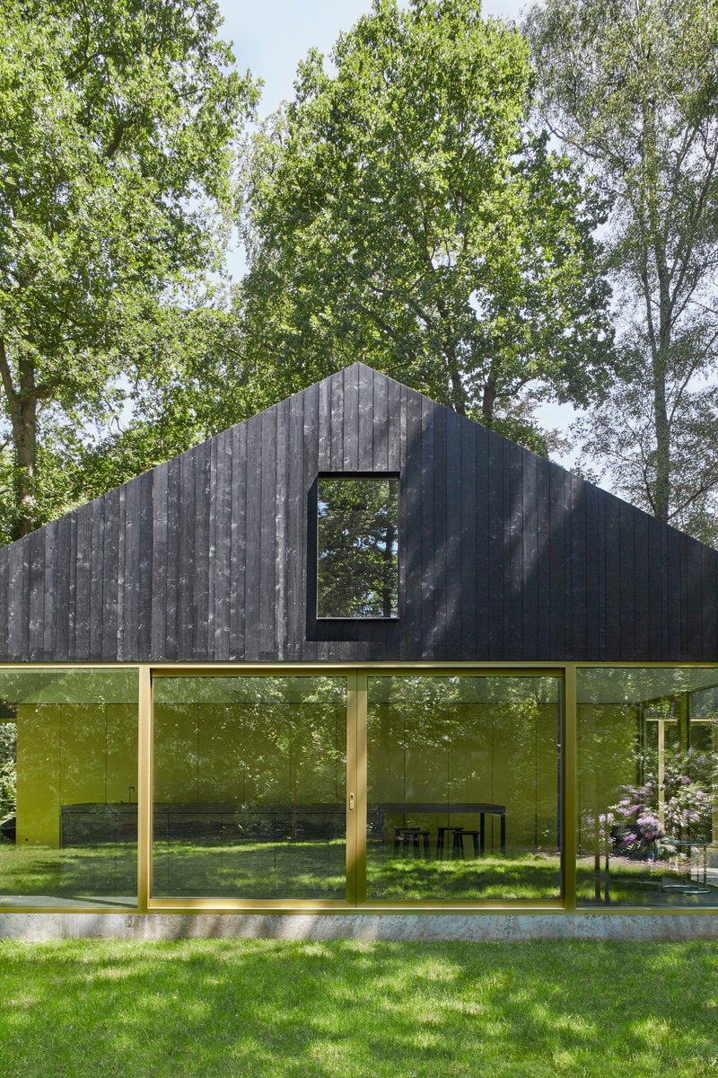 Charred vertical timber facade with a large square window cutout above continuous floor-to-ceiling glazing