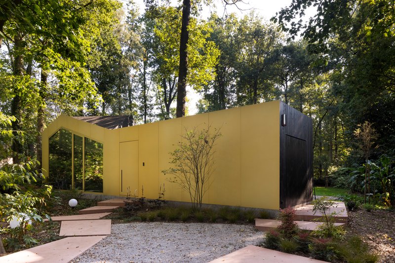 Yellow wall projecting into a gravel garden with curved entry steps and low planted beds