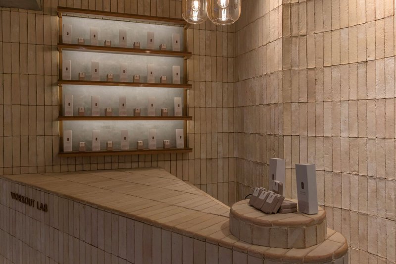Reception counter with pale wood tile cladding and backlit shelves holding product bottles