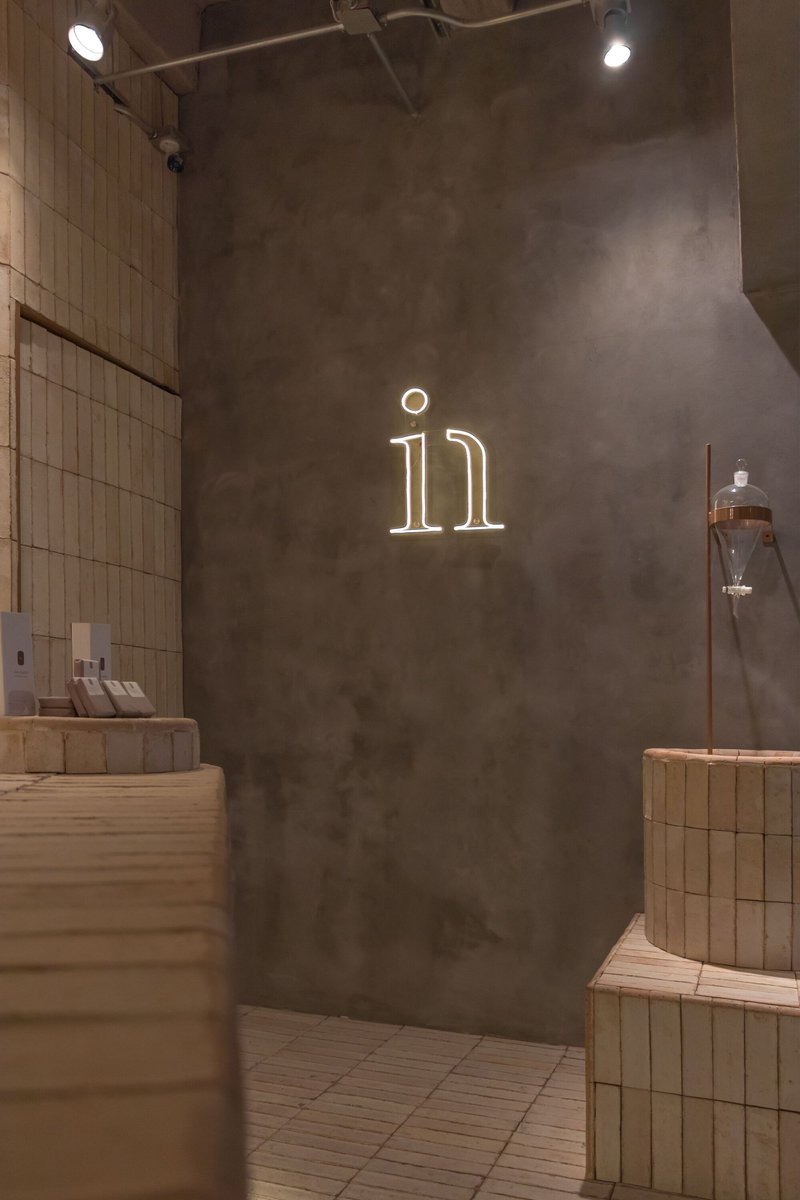 Interior salon corner with neon signage on grey plaster wall and vertical tile panels under track lighting