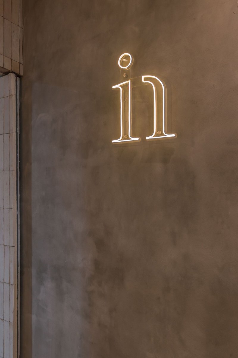 White neon logo mounted on textured grey plaster wall beside vertical tile surface