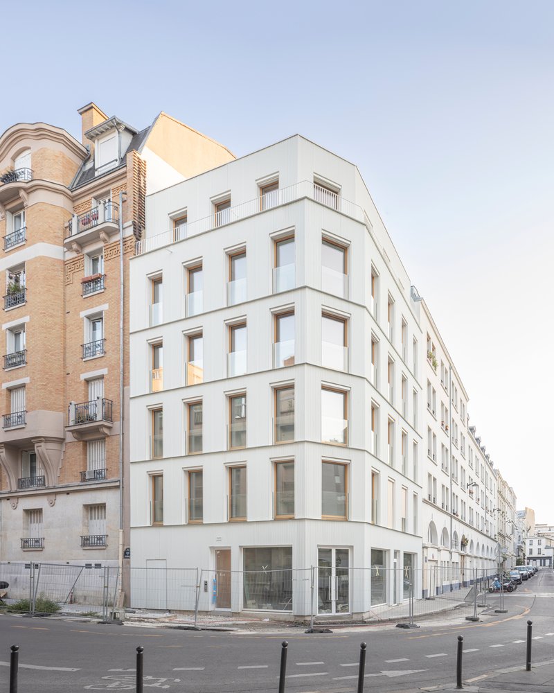White facade with recessed timber-framed windows wrapping around the street corner at daylight