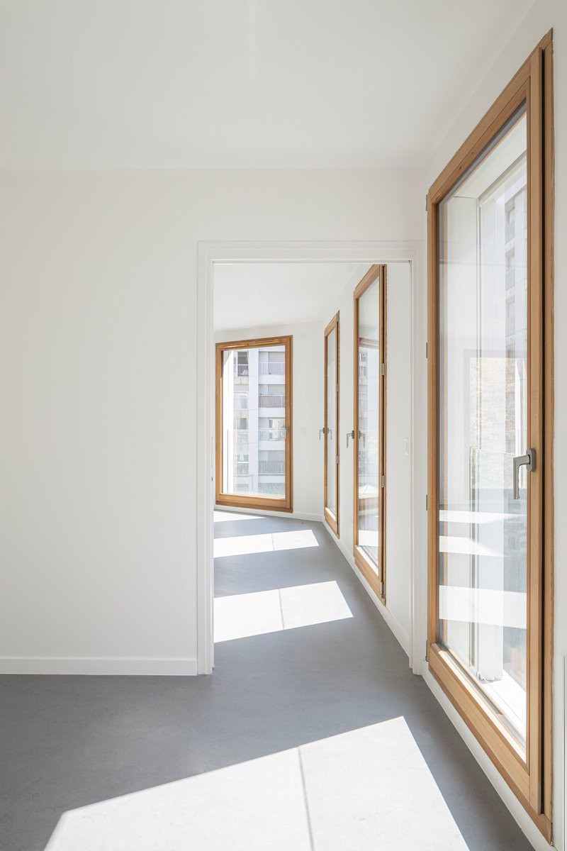 Corridor with timber-framed casement windows creating angled patches of sunlight on the grey floor