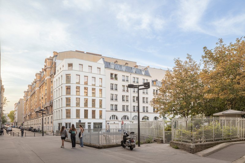Street view of white residential block with pedestrians walking past white picket fence and mature trees in autumn