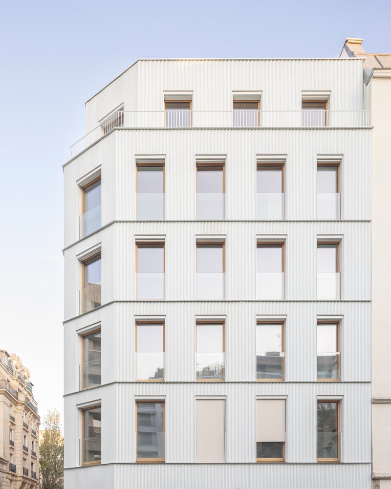 Facade detail showing vertical corrugated cladding panels with timber-framed windows in a regular grid