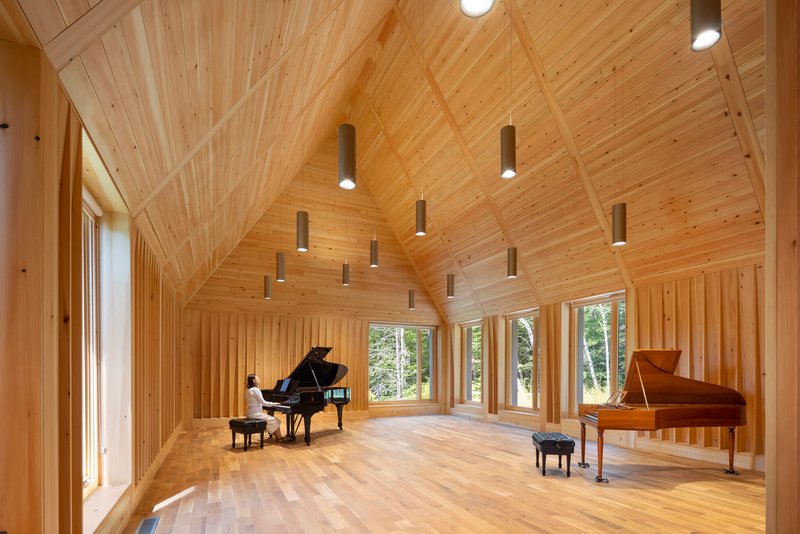 Interior of a timber-lined rehearsal hall with vaulted ceiling and pendant lights above two grand pianos