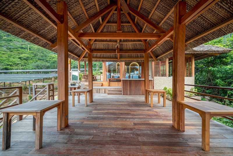 Open timber pavilion with thatched roof, exposed rafters and wooden benches on a raised deck
