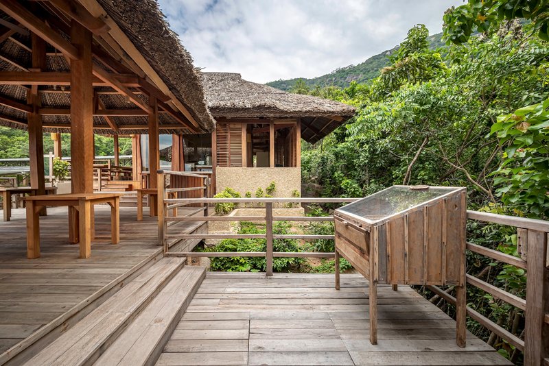 Wooden deck railing and terraced steps leading toward a thatched roof pavilion with green hillside backdrop