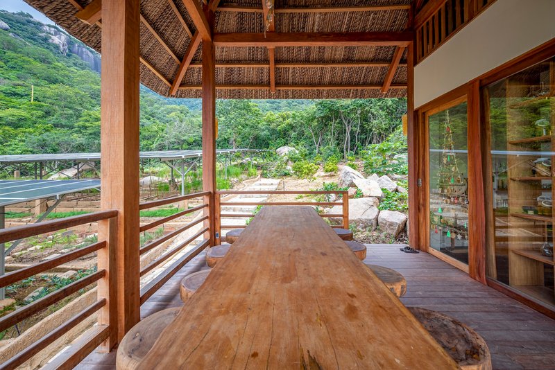 Covered terrace with woven bamboo ceiling and timber columns framing a live-edge table overlooking green hills