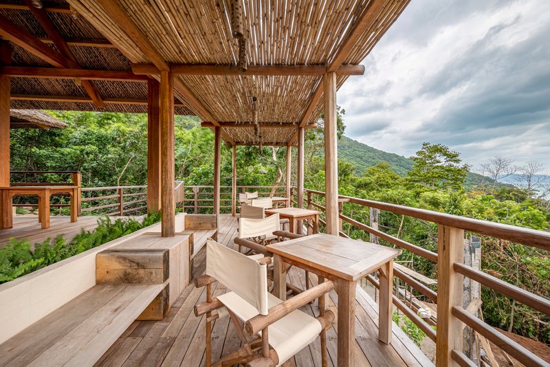 Open-air dining terrace with timber furniture and horizontal rail balustrade under a bamboo-lined roof structure
