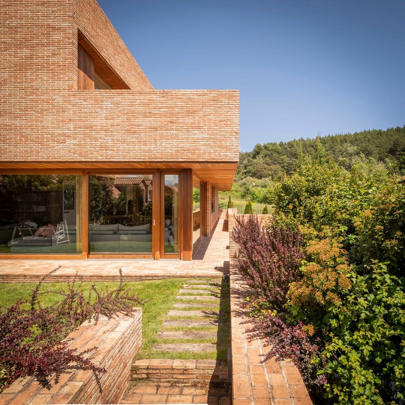 Garden view showing timber-framed glazing beneath brick volumes and stepping stones through planted beds