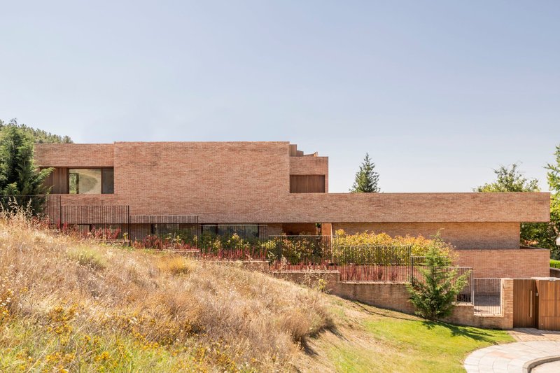 Stepped brick facade with planted terraces descending a sloped site with dry grasses
