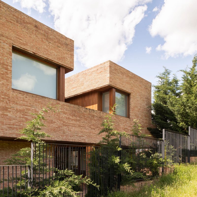 Stacked brick volumes with timber window recesses above a metal railing and young trees